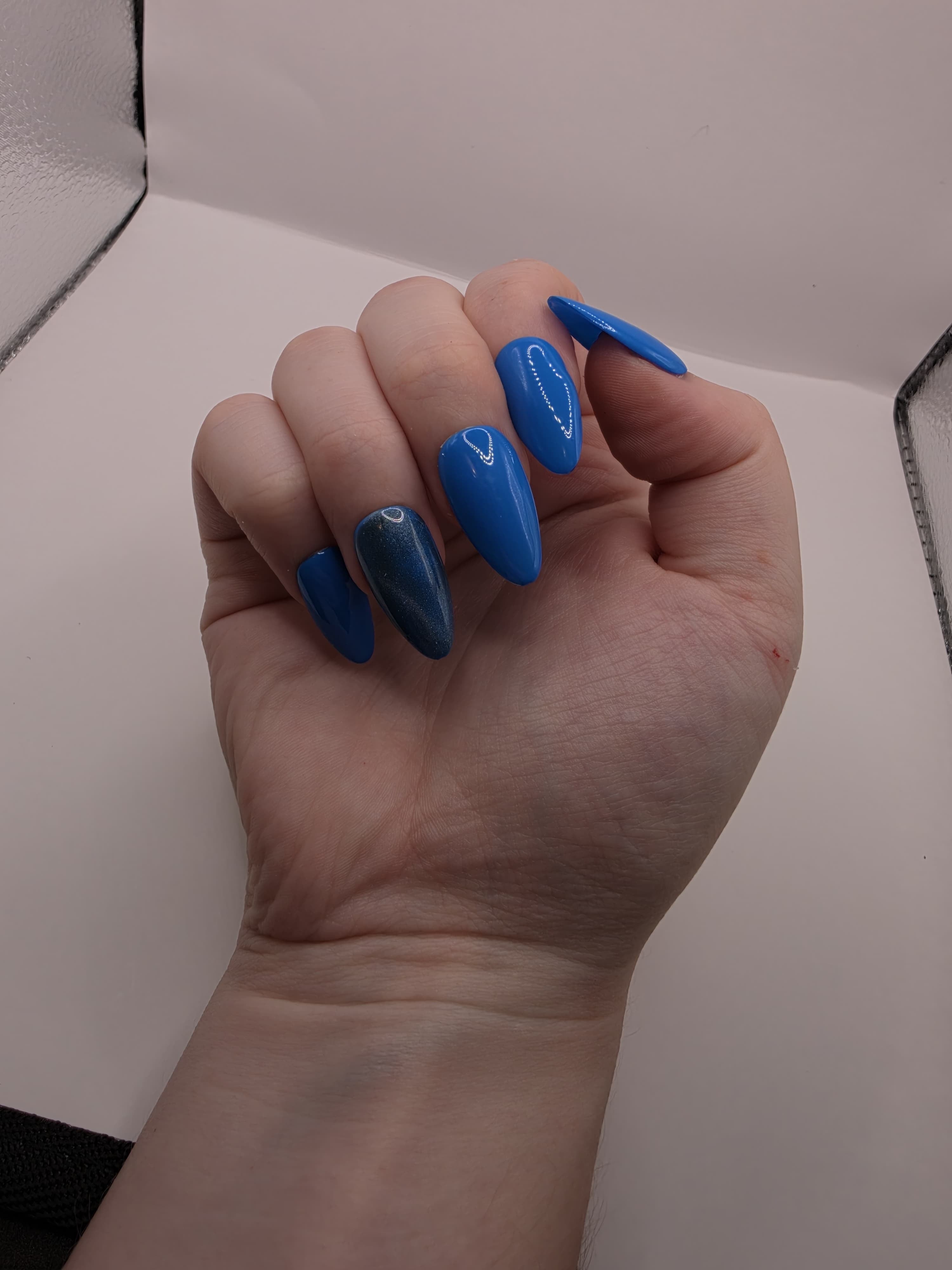 #141 Base Coat with #210 accent nail (catseye): A striking dark sky blue base color with an accent nail on the ring fingers featuring a glittery silver diagonal catseye displayed on medium length almond nails