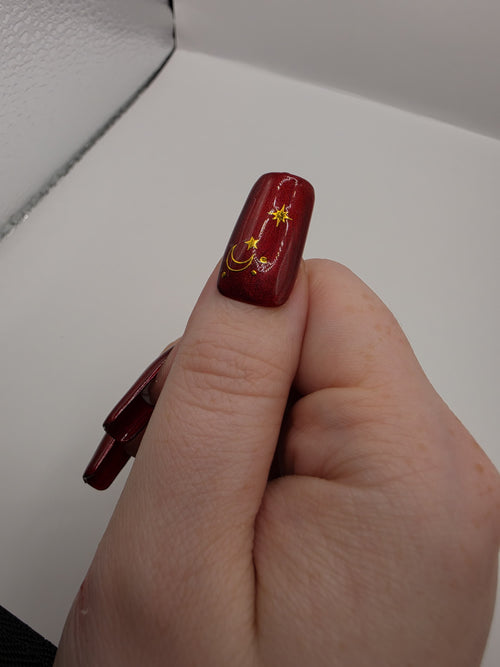 #59 Base Coat: Red shimmer base coat with black opalescent gem on ring fingers and gold moon and star motiff on the thumbs featured on medium square nails