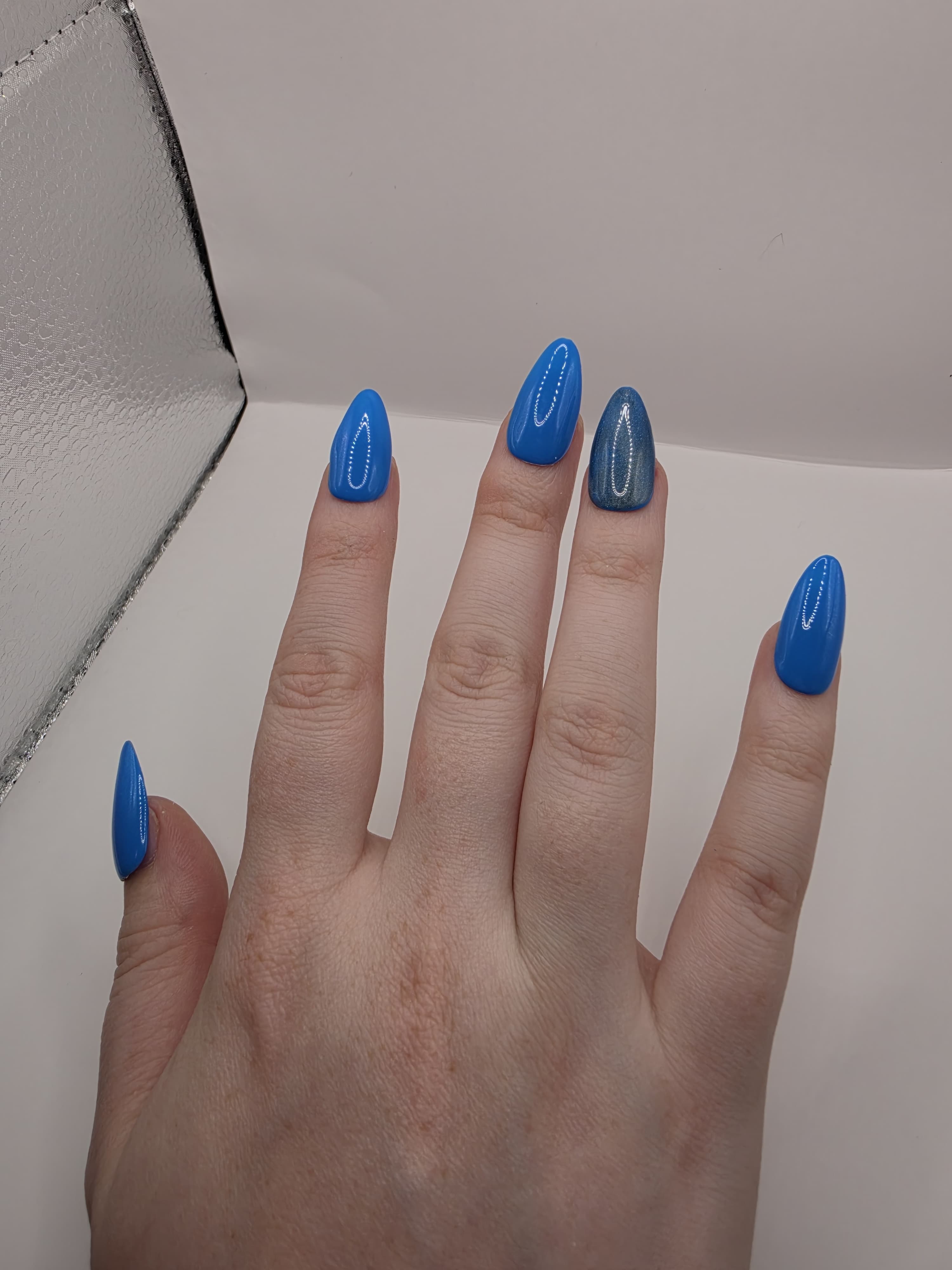 #141 Base Coat with #210 accent nail (catseye): A striking dark sky blue base color with an accent nail on the ring fingers featuring a glittery silver diagonal catseye displayed on medium length almond nails
