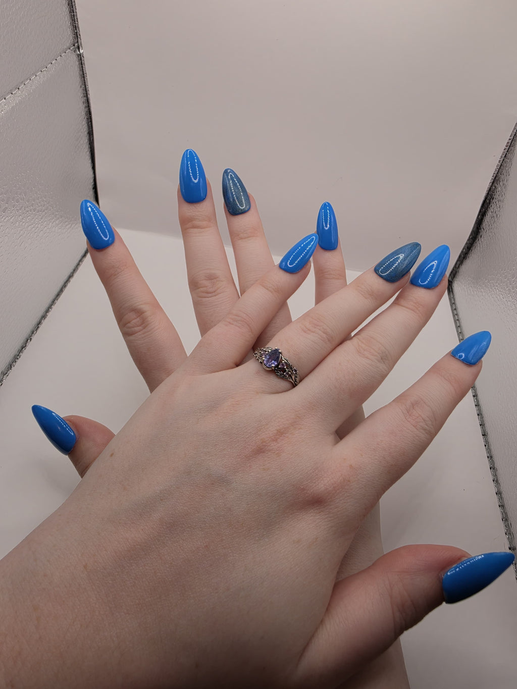 #141 Base Coat with #210 accent nail (catseye): A striking dark sky blue base color with an accent nail on the ring fingers featuring a glittery silver diagonal catseye displayed on medium length almond nails